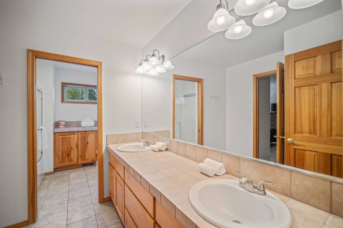 A serene bathroom featuring double vanity sinks, a large mirror, and wooden cabinetry. The space is light-filled and spa-like, designed for both relaxation and efficient group routines.