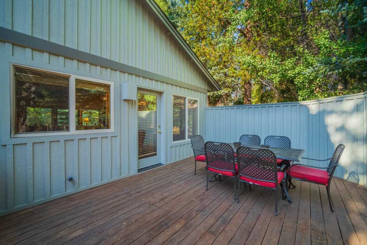 An inviting patio set with a table and chairs sits nestled among tall trees next to the exterior of the home, suggesting a seamless transition from indoor comfort to outdoor relaxation and adventure.