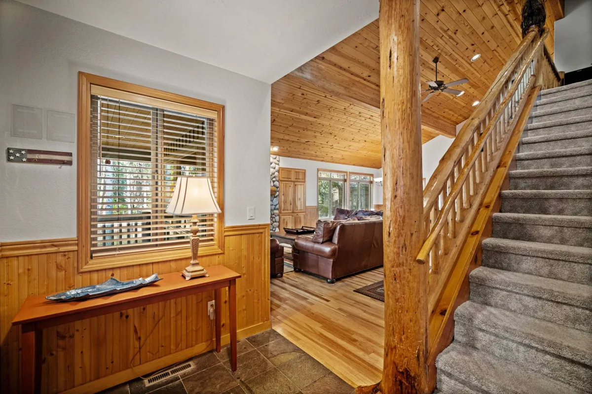 A cozy entryway scene with a staircase, a wooden table, a lamp, and a seating area by a large window. Natural light floods in, creating a welcoming atmosphere that bridges the indoors with the outdoors.