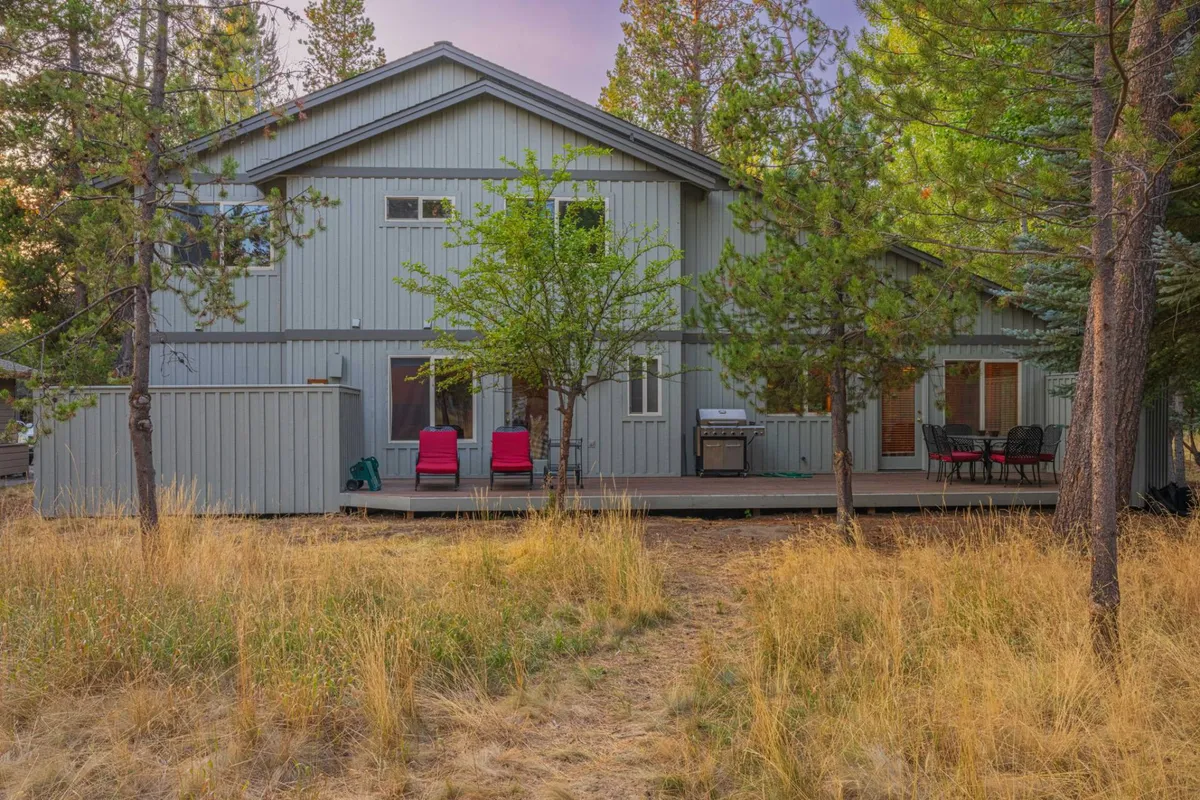A tranquil scene of a wooden deck with two pink chairs, a grill, and lush green trees creating an inviting atmosphere for relaxation or gatherings.