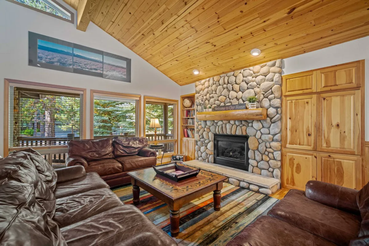 A warm interior featuring a stone fireplace, leather sofas, a wooden coffee table, and expansive windows. The space is ideal for family gatherings or planning the next adventure together, embodying a welcoming and restorative atmosphere.