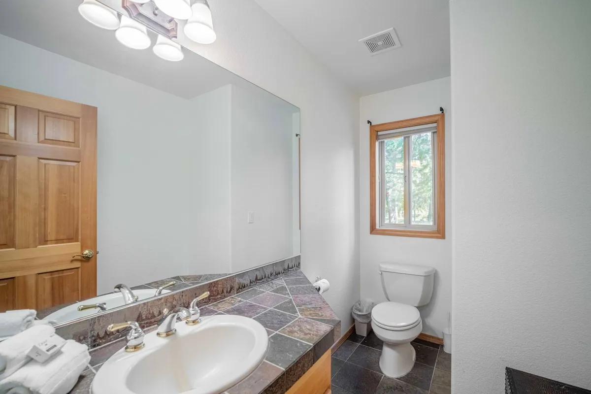 A modern bathroom with double sinks, a large mirror, a window providing natural light, and a wooden door. The ambiance is calm and refreshing, ideal for morning routines or unwinding after a busy day.