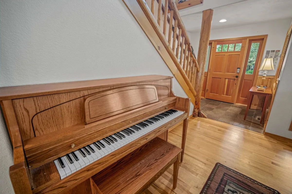 This image captures the entryway of the home, including a prominent view of the front door, staircase, and a piano. Natural light filters in, welcoming guests and suggesting a sense of arrival. The piano and lamp evoke a sense of warmth and history, while the front door connects viewers with the idea of entering or exploring the property.