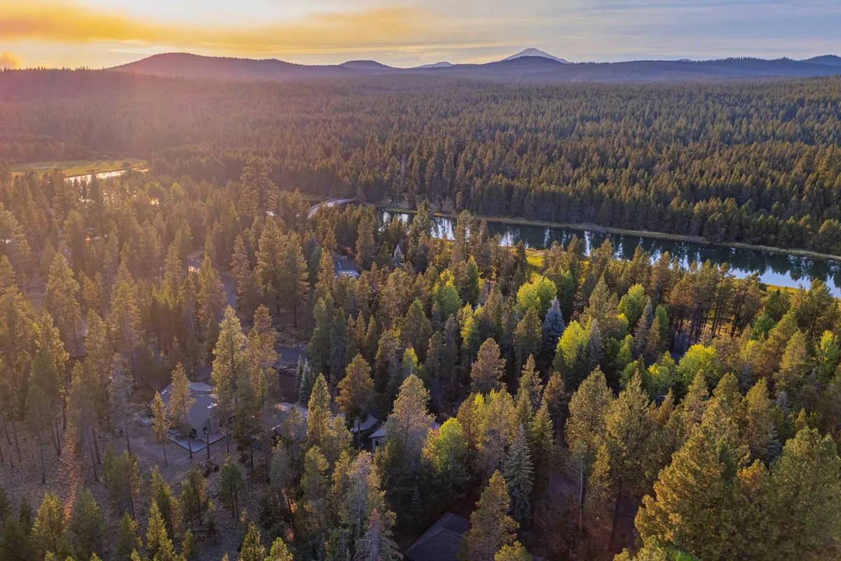 A panoramic view of Sunriver’s natural landscape, featuring a dense forest, a meandering river, and mountains illuminated by a warm sunset glow. The scene evokes tranquility and the inviting sense of adventure found on local trails and along the water’s edge.