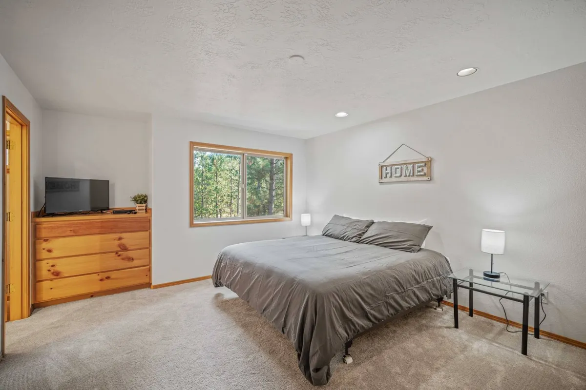 A bright, comfortable bedroom featuring a plush bed draped in fresh bedding, a nightstand, dresser, and a window letting in natural light. The decor is calm and restful, creating an inviting space for relaxation after a day of adventure.