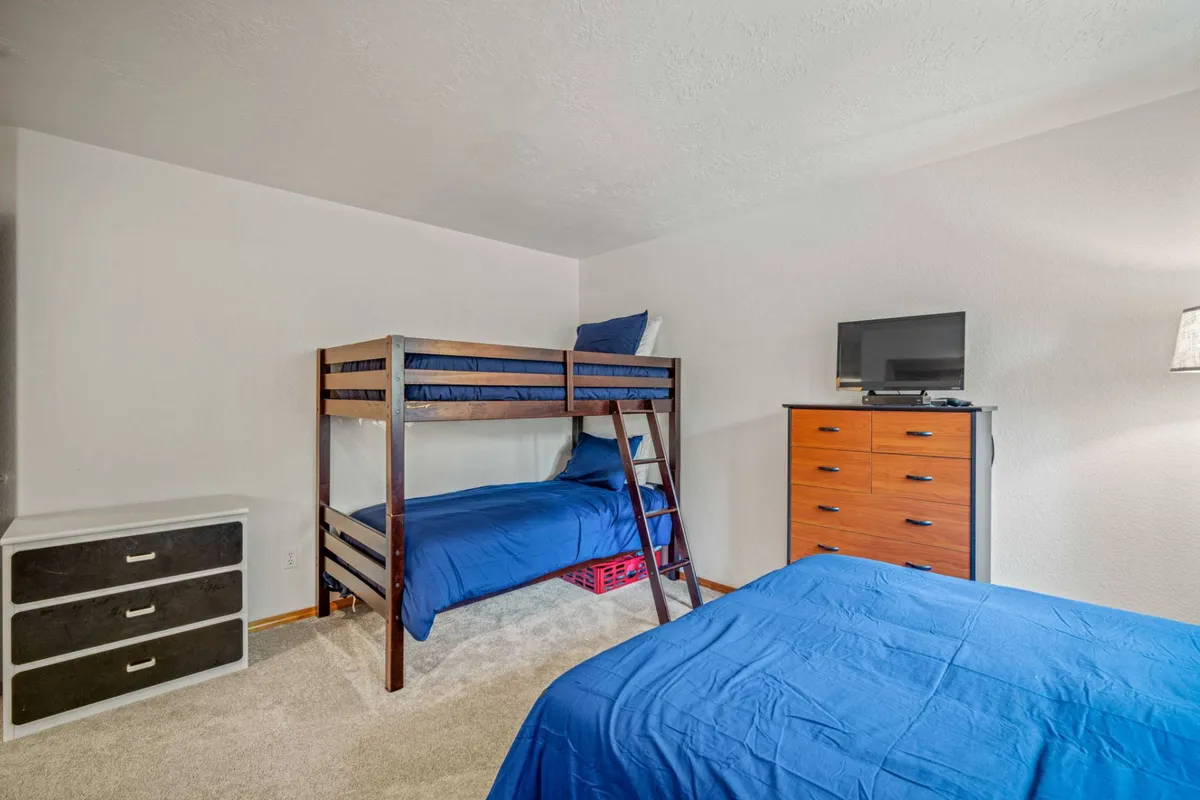 A spacious bunk room containing a bunk bed, two single beds, a dresser, and a TV. The layout is playful and practical, ideal for families or groups, with a cozy mood suitable for movie nights and bedtime stories.